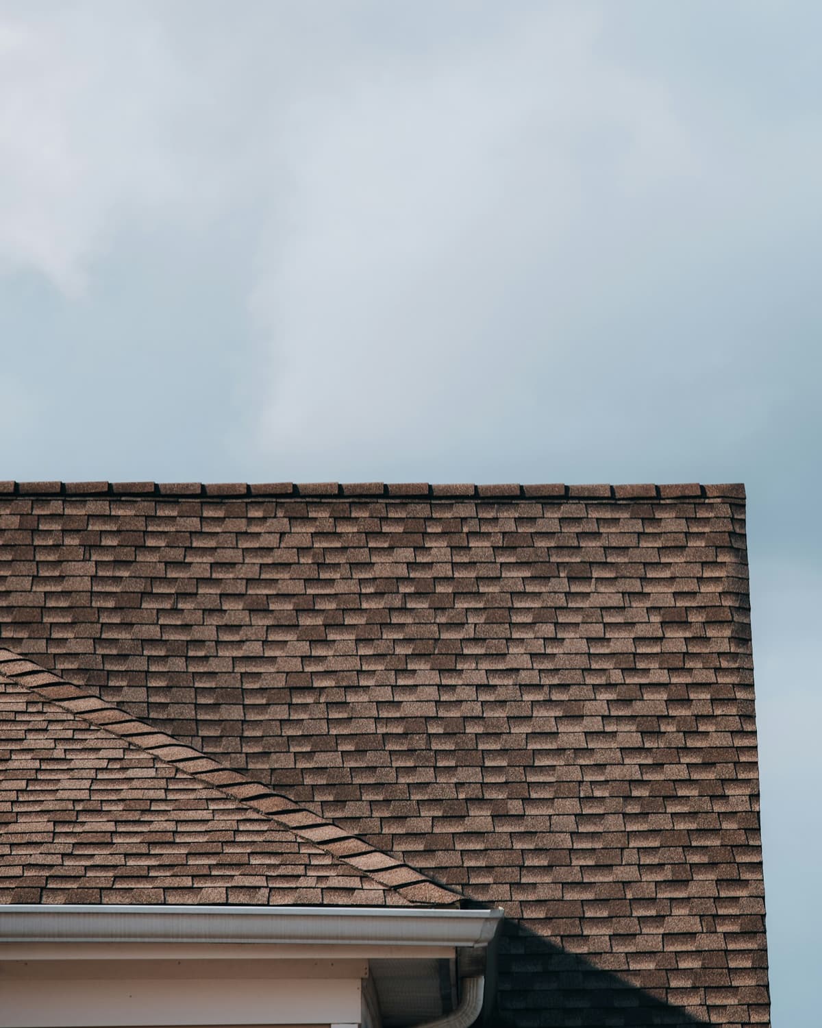 Close-up of a brown architectural asphalt-shingle roof gable with white trim against a cloudy sky
